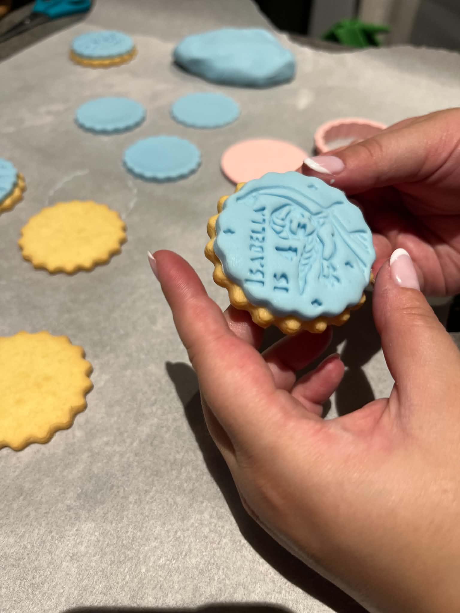 A blue iced biscuit being decorated by hand alongside other biscuit shapes.