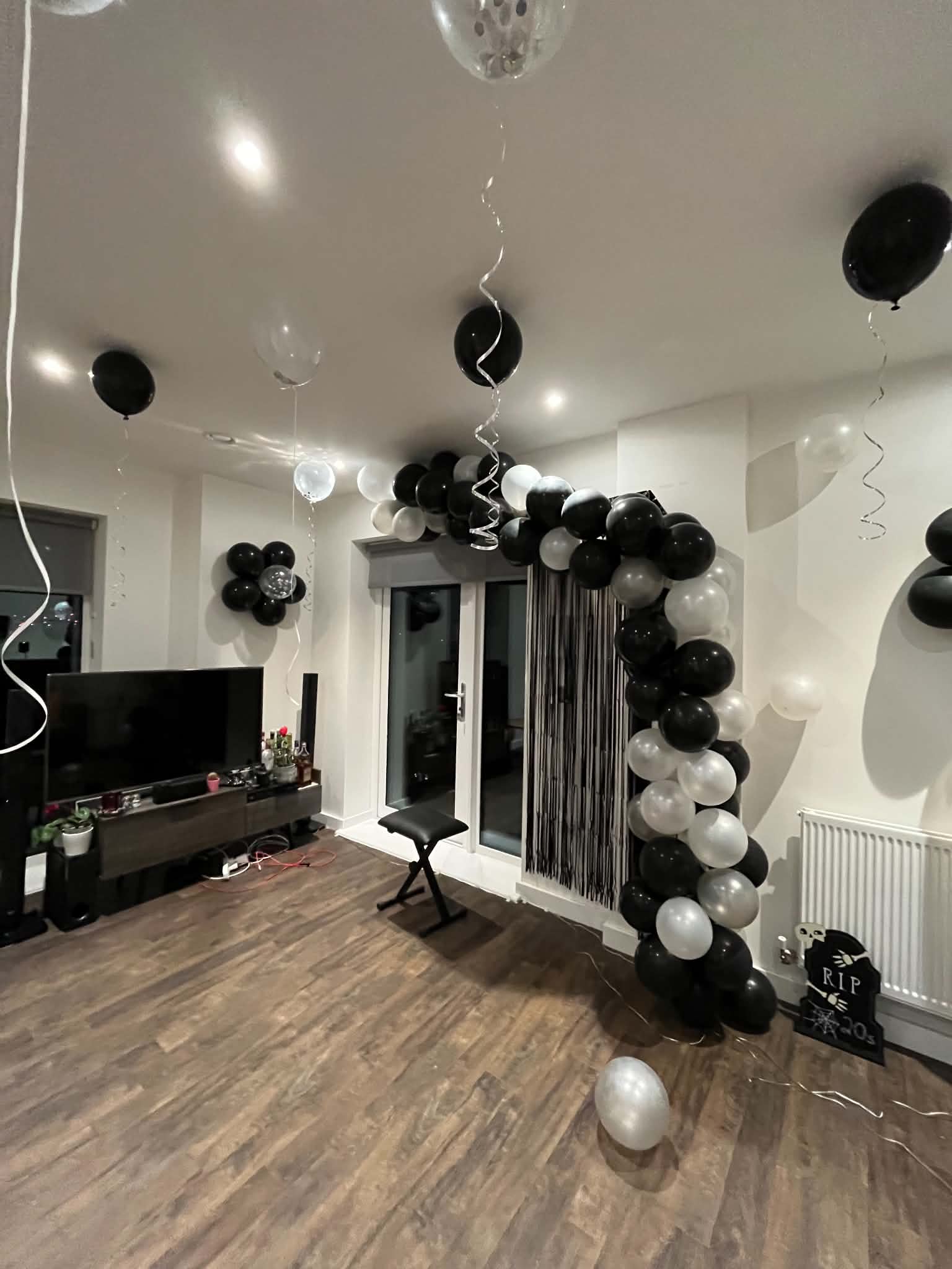 Black, white, and silver balloon arch arranged around a doorway for a party setup.